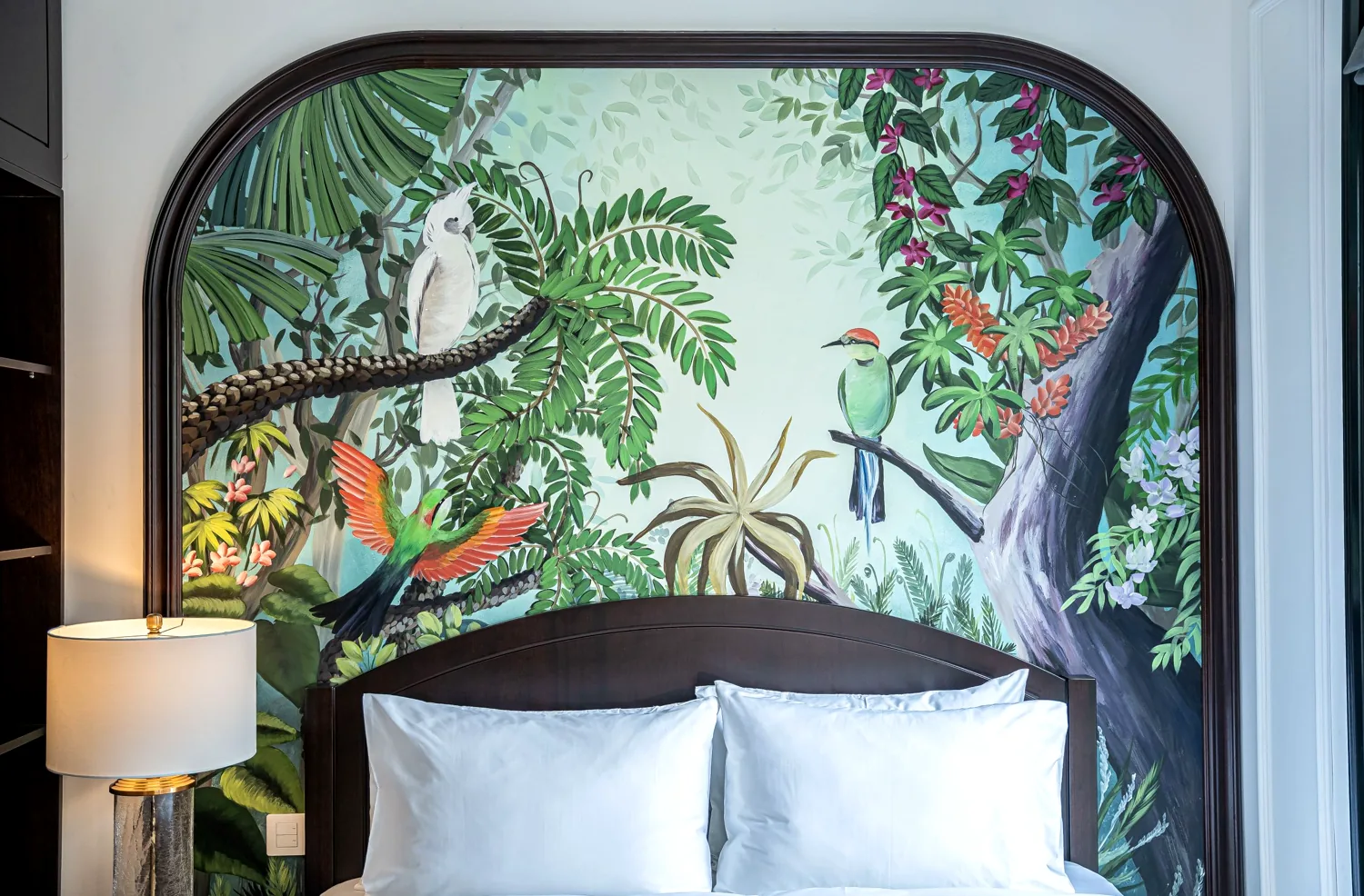Hand-painted arched tropical-bird mural headboard above a king bed